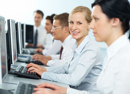 A businesswoman typing among her colleagues, looking at camera and smiling